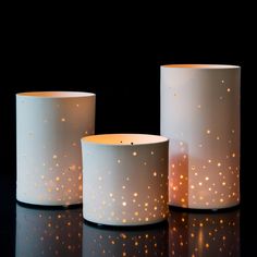 three lit candles sitting on top of a black table next to each other with gold dots all over them