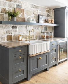 a kitchen with gray cabinets and stone wall behind the sink, along with open shelving