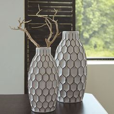 two white vases sitting on top of a table next to a window with blinds