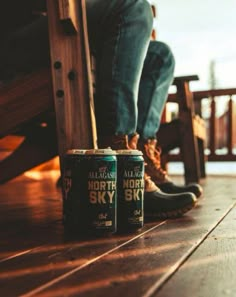 two cans of beer sitting on top of a wooden floor next to a person's feet