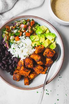 a white plate topped with chicken, rice and black beans next to a bowl of guacamole