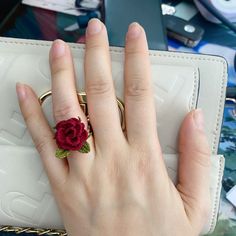 a woman's hand holding a ring with a flower on it and a white purse