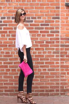 a woman standing in front of a brick wall holding a pink purse and wearing black pants