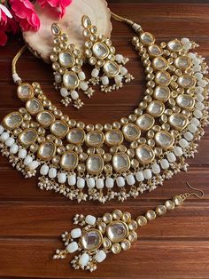 a necklace and earring set on a wooden surface with flowers in the background,