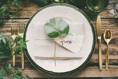 a table setting with place cards and silverware on it, along with greenery