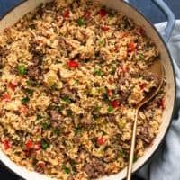 a large pot filled with rice and meat on top of a table next to a wooden spoon