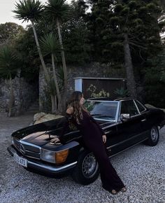 a woman leaning on the hood of a black mercedes parked in front of a house