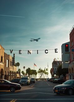 an airplane is flying over the street with cars parked on the side walk and palm trees