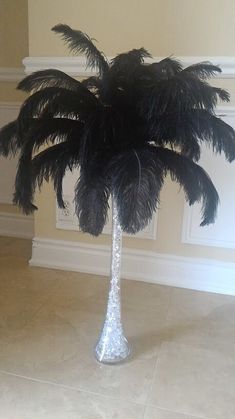 a tall palm tree with black feathers in a vase on the floor next to a wall