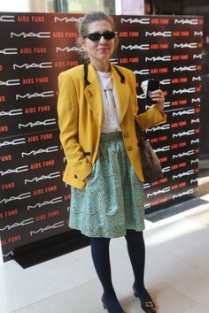 a woman standing in front of a wall holding a cell phone and wearing a yellow blazer