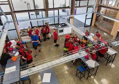 a group of people in red shirts are gathered around tables and chairs inside an open building