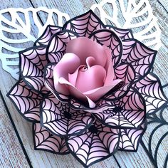 a pink rose is sitting in the center of a spider web paper sculpture on a wooden table