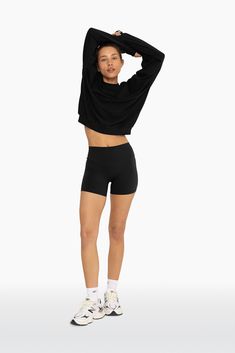 a woman in black shorts and crop top posing for the camera with her hands on her head