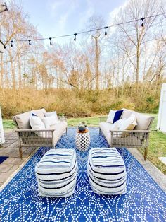 two chairs and a ottoman on a blue rug in front of a white house with string lights