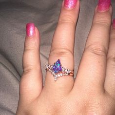 a woman's hand with pink nail polish holding a purple and white diamond ring