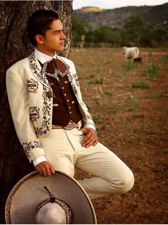 a man in a white suit and hat leaning against a tree