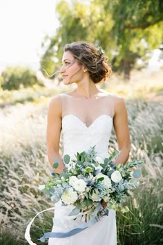 a woman in a wedding dress holding a bridal bouquet with greenery and flowers