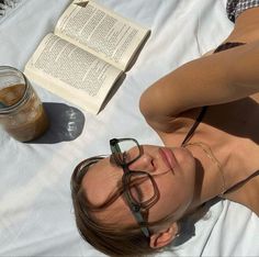 a woman laying on top of a white blanket next to an open book and drink