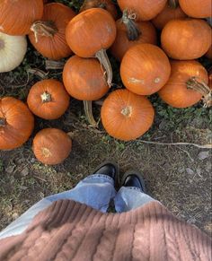 a person standing next to a pile of pumpkins on the ground with their feet up