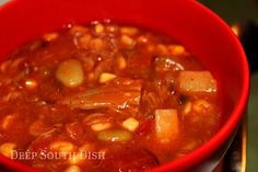 a red bowl filled with beans and meat soup on top of a stove burner