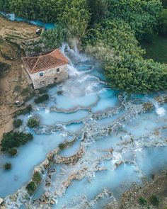 an aerial view of a river running through a lush green forest next to a stone building