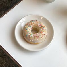 a white plate topped with a donut covered in frosting and sprinkles