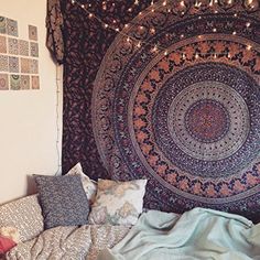 a large tapestry hanging on the wall above a bed with pillows and blankets in front of it