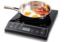 a frying pan with eggs and bacon cooking on top of an electric cooktop