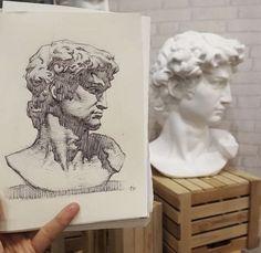 a person holding up a drawing in front of some busts