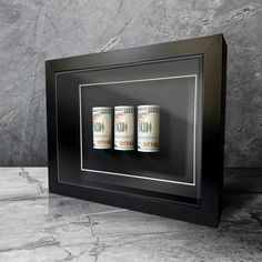 three stacks of one hundred dollar bills in a black frame on a marble countertop