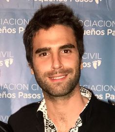 a man in black shirt standing next to a blue wall and smiling at the camera