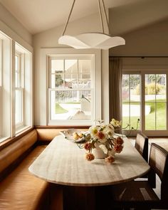 a dining room table with flowers on it in front of two large windows that look out onto the yard