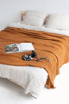 a bed with an orange blanket on top of it and a book next to it