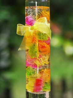 a tall glass filled with gummy bears on top of a wooden table next to trees