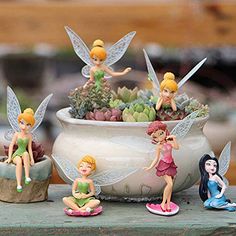 some little fairy figurines are sitting in a pot with succulents