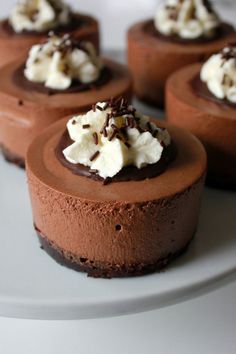 chocolate cheesecakes with whipped cream on top are sitting on a white platter