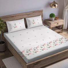 a bed with white sheets and pink flowers on the bottom, along with two nightstands