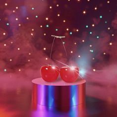 two cherries sitting on top of a metal object in front of a colorful background