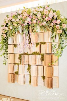 an arrangement of books with flowers and greenery on the wall above it is decorated with pink roses