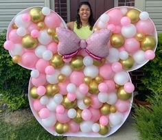 a woman standing in front of a minnie mouse balloon wall with pink, white and gold balloons