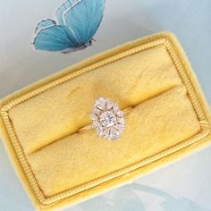 a diamond ring sitting on top of a yellow velvet case next to a blue butterfly