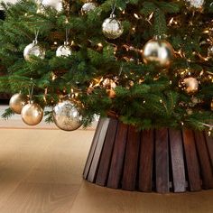 a christmas tree with gold and silver ornaments in a wooden basket on the floor next to a fireplace