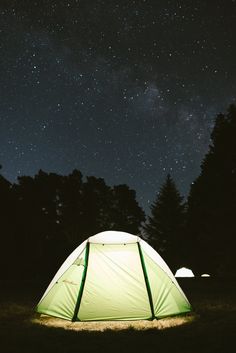 a green and white tent sitting on top of a lush green field under a night sky filled with stars