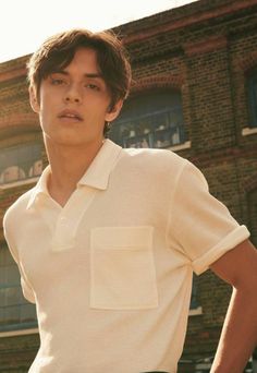 a young man standing in front of a brick building with his hands on his hips