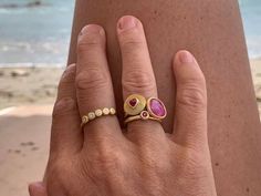 a woman's hand with two rings on it and the beach in the background