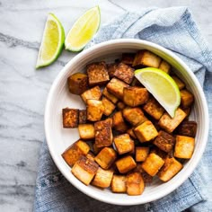 a white bowl filled with cubed tofu next to two lime wedges on a blue towel