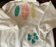 a white sweatshirt with colorful surfboards embroidered on the front and back, sitting on a couch