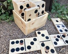 several wooden blocks with black dots on them sitting in the gravel near some plants and flowers