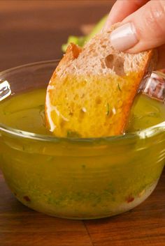 a person dipping something into a small bowl with bread in it on a wooden table