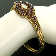 You are looking at a vintage piece crafted in solid 14k yellow gold. The bangle features a gorgeous open work design topped with 12 oval shaped amethyst stones. Each amethyst is prong set on top of an open work designed basket. A marquise shaped cabochon opal sits at the center of the bangle adding amazing color with its green and blue play. The bangle itself features a brick-like texture throughout its solid construction and its original patina has been preserved which can be polished off to ma Montclair Nj, Amethyst Stones, Work Design, Amethyst Stone, Green And Blue, Bangle Bracelet, Prong Setting, Bangle Bracelets, Patina